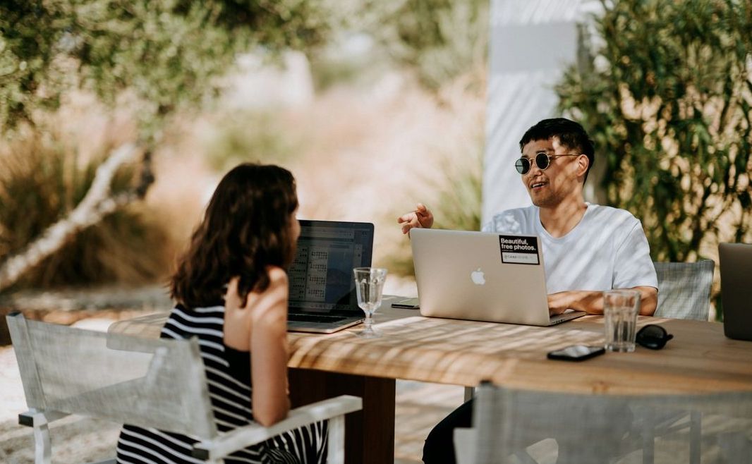 Two people working remotely together outdoors at a table